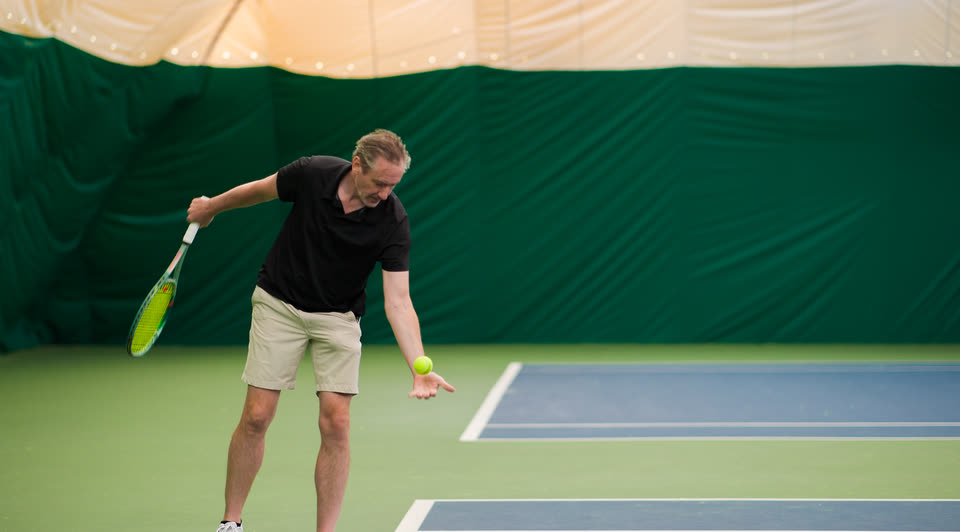 A player tossing the ball up to serve on an indoor court at Match Point KC